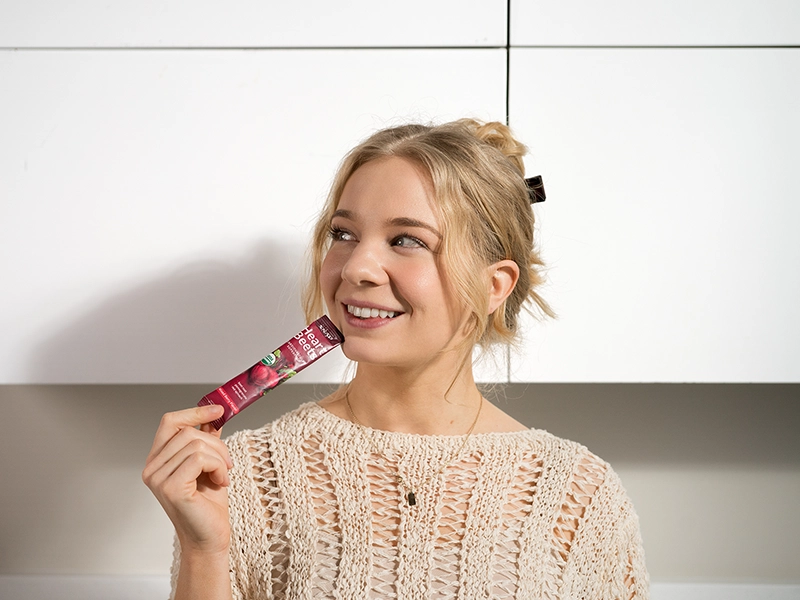 A retouched photo of a woman holding a Snap Supplements soft-pack at home. Retouched photo shoot for an advertising campaign.
