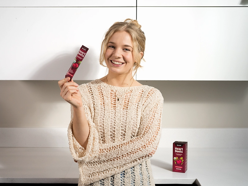 A retouched photo of a woman holding a Snap Supplements soft-pack at home. Retouched photo shoot for an advertising campaign.