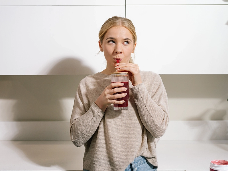A retouched photo of a girl drinking a vitamin cocktail from a glass. Influencer retouching for an advertising campaign for a dietary supplement brand.