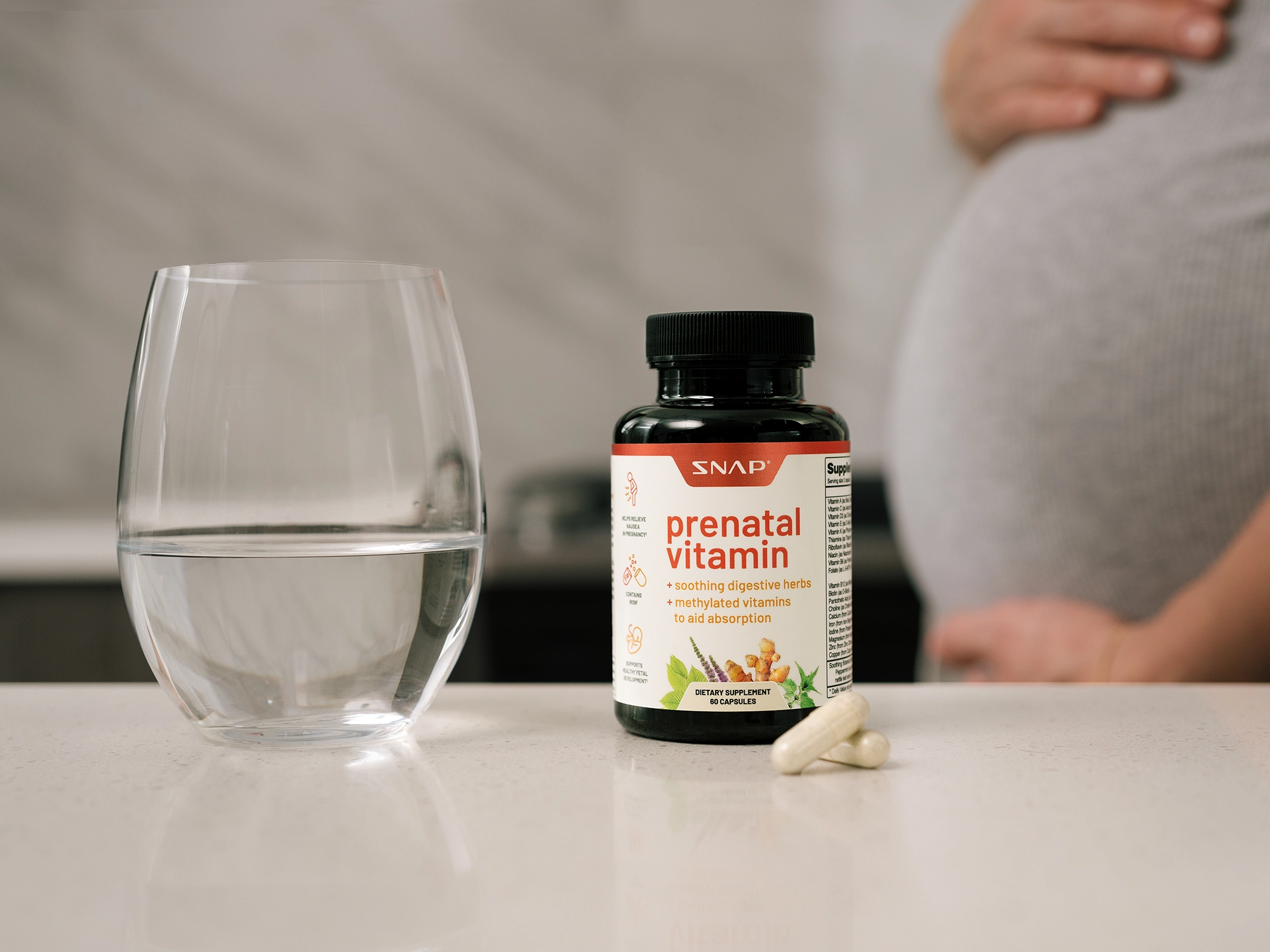 A retouched photo of a jar of vitamins on a table and a glass of water on the table. A pregnant woman's belly is in the background. Retouched photo of women's health products.
